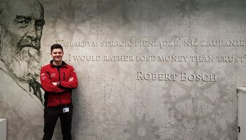 Zdjęcie przedstawia absolwenta UPWr, kierunku Inżynieria Bezpieczeństwa - Marcina Robaka. Stoi na tle ściany z podobizną i cytatem Roberta Boscha o treści: 